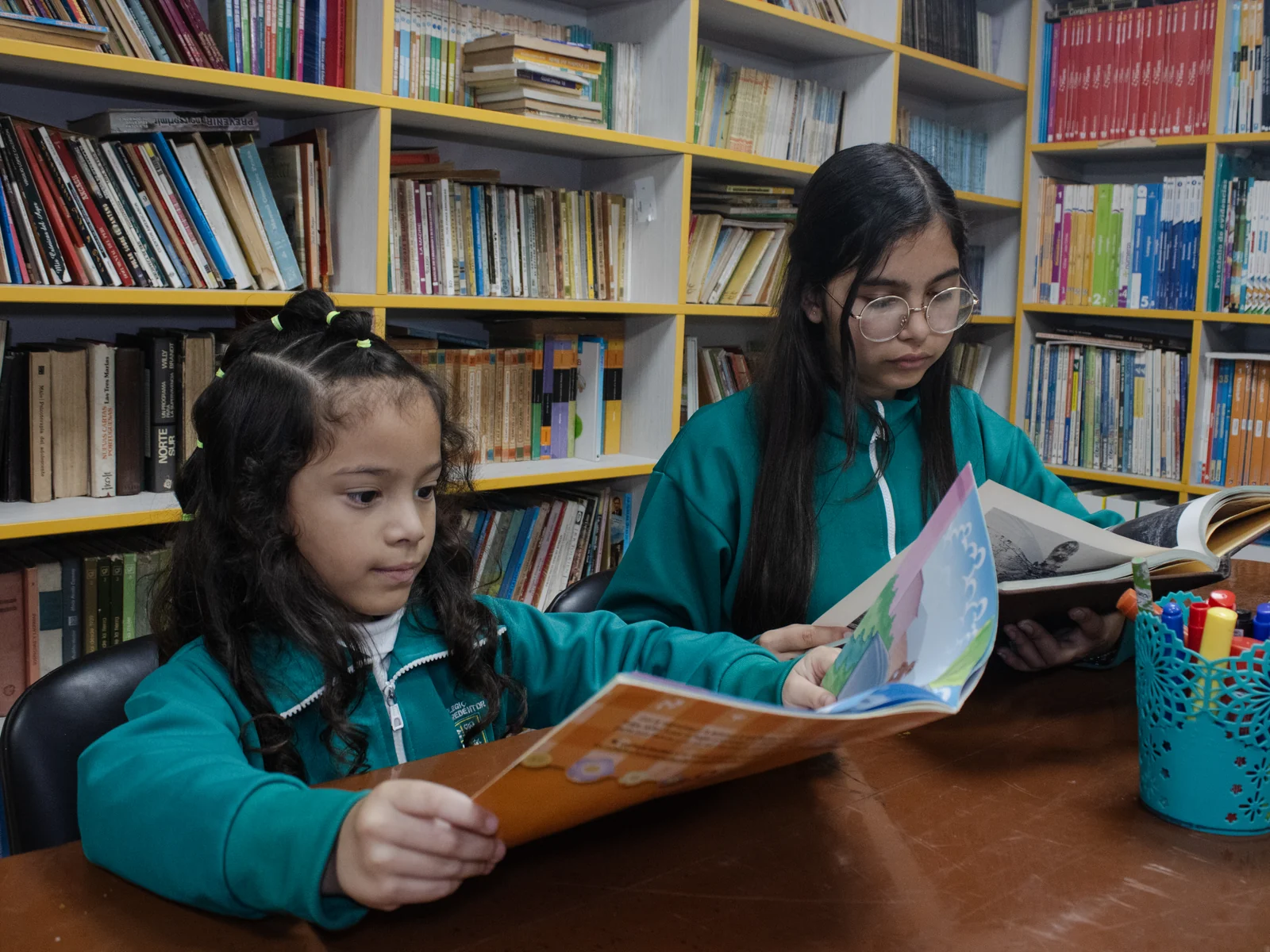 Una estudiante de Secundaria lee junto a una niña de Inicial en la biblioteca.