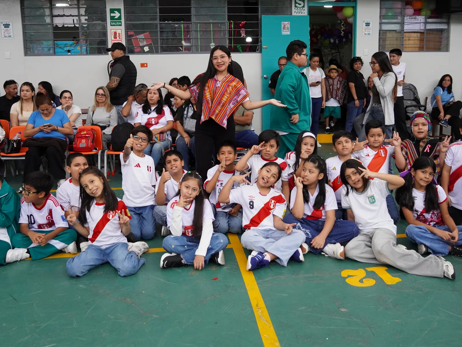 Estudiantes de Primaria posan sentados con su maestra durante la celebración de Fiestas Patrias.