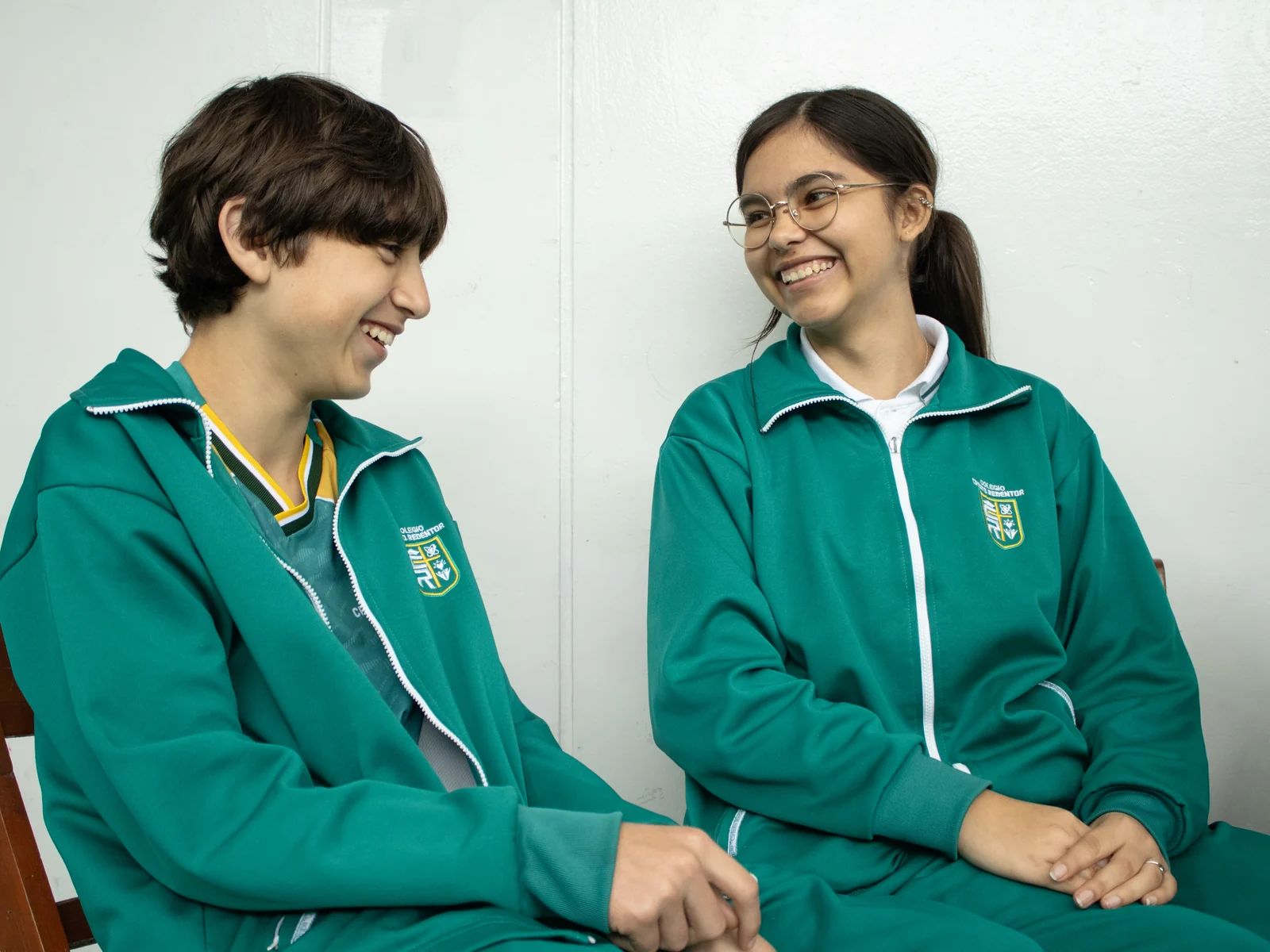 Dos estudiantes de Secundaria conversan y ríen sentados en el colegio.